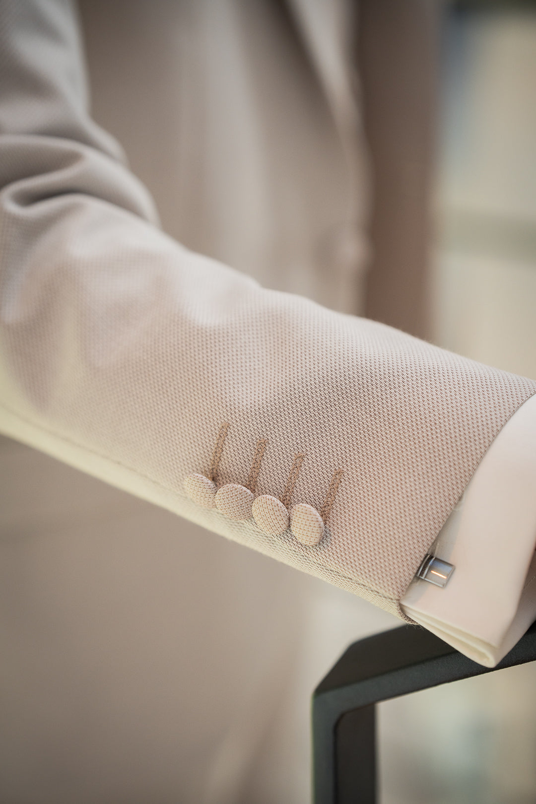 L'image montre le détail d'une manche de costume beige clair avec des boutons de manchette. Les boutons sont de couleur beige clair assortie au costume. La chemise blanche sous la manche est visible.