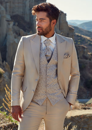 Homme portant un costume de marié beige. La veste et le pantalon sont unis beige et le gilet avec des motifs floraux assorti à une cravate 