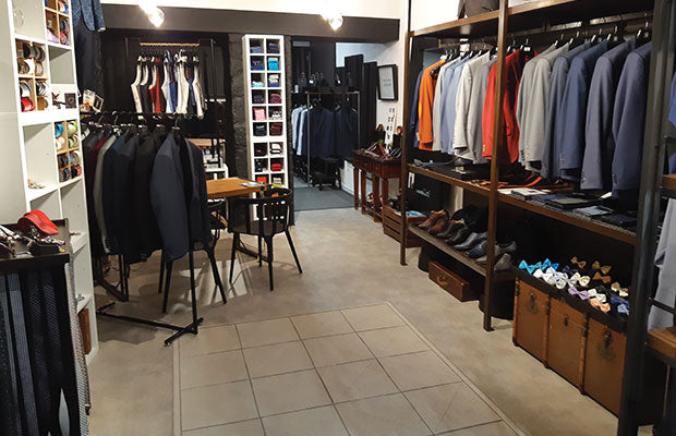 Intérieur d'une boutique de costumes pour homme à Aix-les-Bains. Présentoir de costumes d'affaires, costumes de marié et accessoires de mode (chaussures, nœuds papillons, cravates, pochettes).