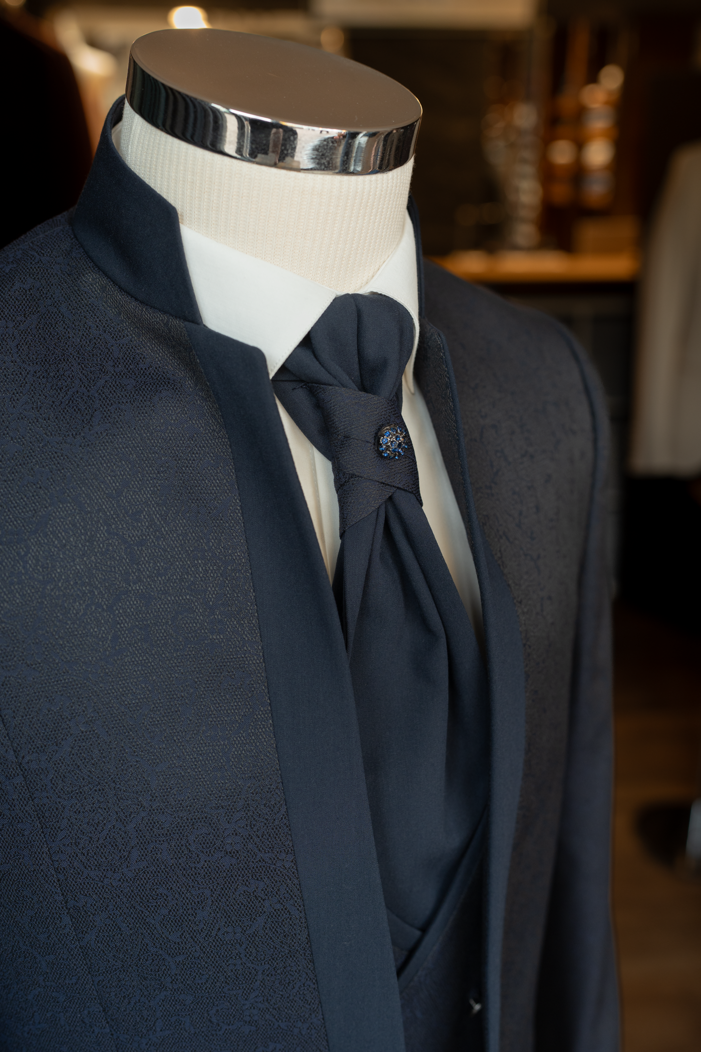 Gros plan sur le col officier (Mao) et la lavallière avec broche bijou bleue sur une chemise blanche.