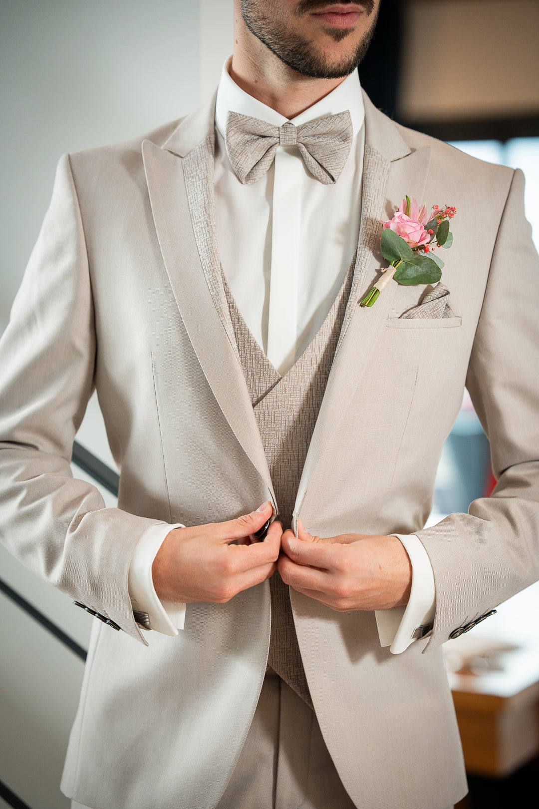 Détail de l'ensemble 3 pièces Mathéo beige, nœud papillon assorti au gilet et à l'empiècement sur le revers du col, boutonnière fleurs rose 