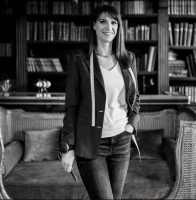 Experte en costumes de mariage et d'affaires. Une femme souriante, mètre de couturière autour du cou, prête à conseiller pour la création de costumes personnalisés.