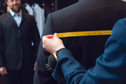 Prise de mesures pour un costume sur mesure. Un tailleur mesure l'épaule d'un client avec un ruban jaune.